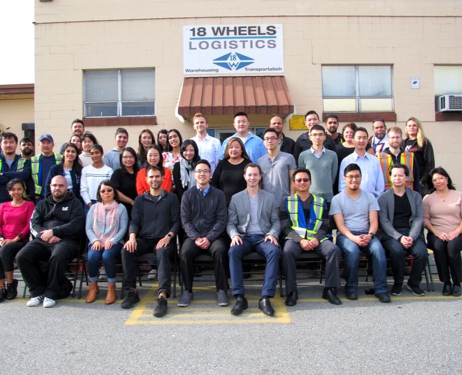 A group photo of the 18 Wheels Logistics team in front of their Burnaby warehouse, highlighting their role as a leading 3PL company.