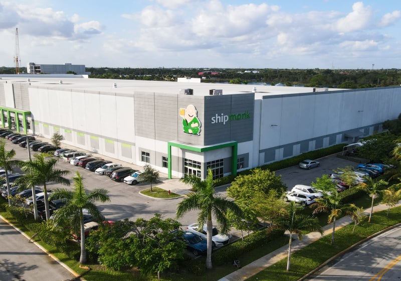 Aerial view of ShipMonk headquarters and warehouse in Florida, showcasing the large 3PL facility surrounded by a landscaped area and palm trees.