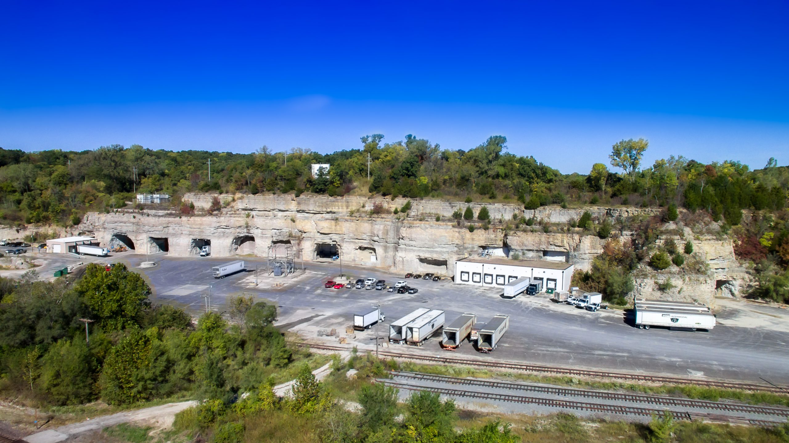 Aerial view of National Cold Storage headquarters and warehouse facility, featuring multiple loading docks and trailers, surrounded by rocky landscape and greenery.
