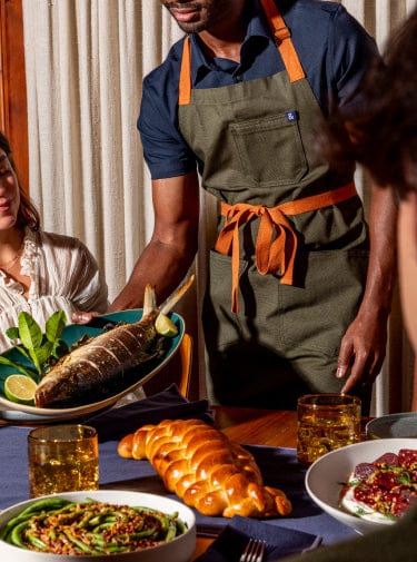Hedley and Bennett presents a bold, chef-focused brand identity with a rustic yet premium aesthetic. The main hero image features their signature tagline 'LIFETIME GUARANTEE Damn Good Aprons' with 'DESIGNED BY CHEFS' prominently displayed, emphasizing their professional culinary credentials. The homepage showcases a grid layout of their best-selling aprons in various colors and patterns, including solid colors like Midnight Blue and Olive Green, as well as designer collaborations with Rifle Paper Co., Disney's Ratatouille, LoveShackFancy, and MLB teams. The product photography is clean and consistent, featuring aprons laid flat against neutral backgrounds. The overall design combines a modern e-commerce layout with artisanal craftsmanship messaging, using a mix of typography styles that balance professionalism with approachability. The color palette spans from earth tones to vibrant patterns, reflecting the brand's versatility in serving both professional kitchens and home cooks.