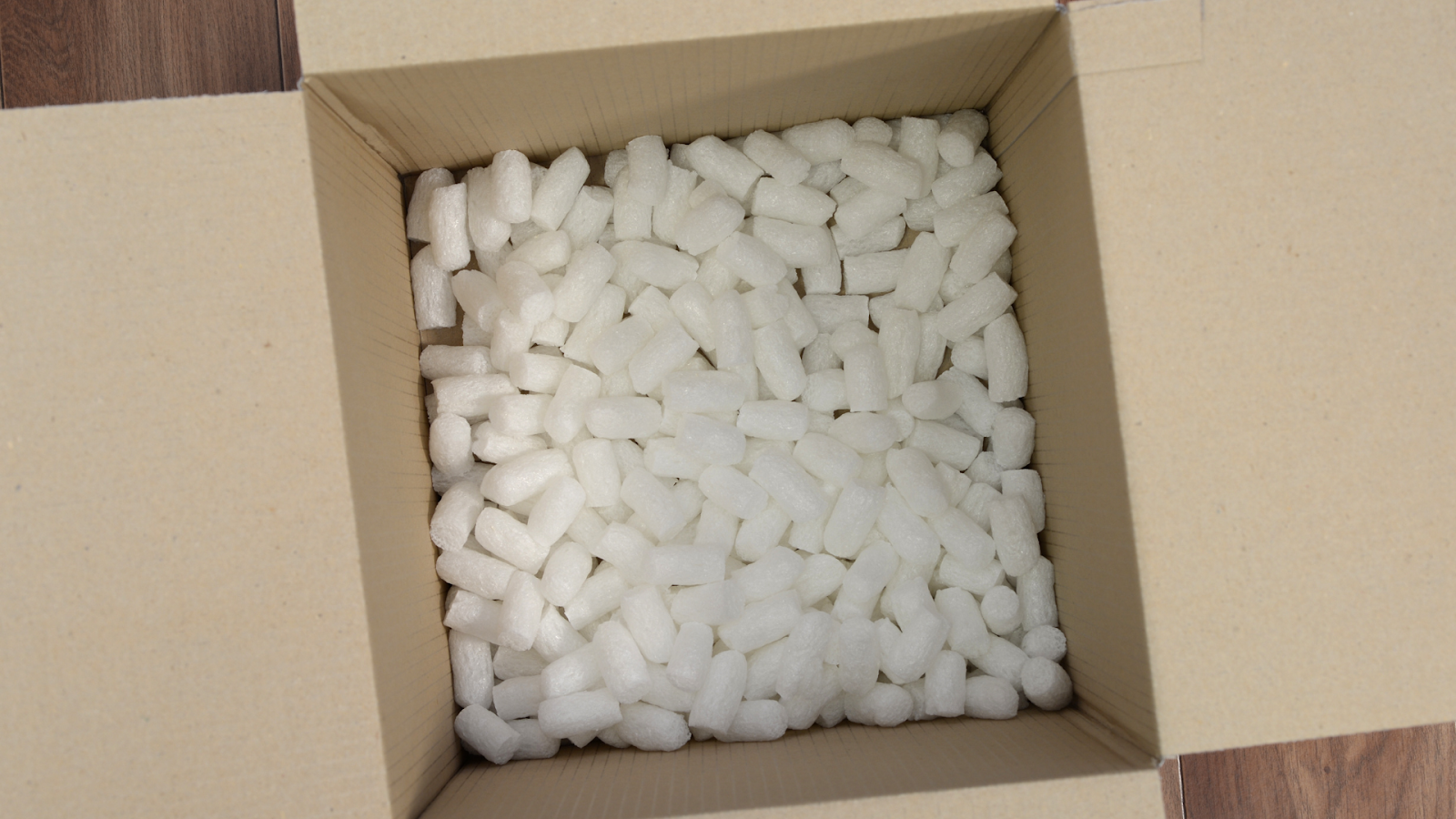 An open cardboard shipping box filled with white packing peanuts